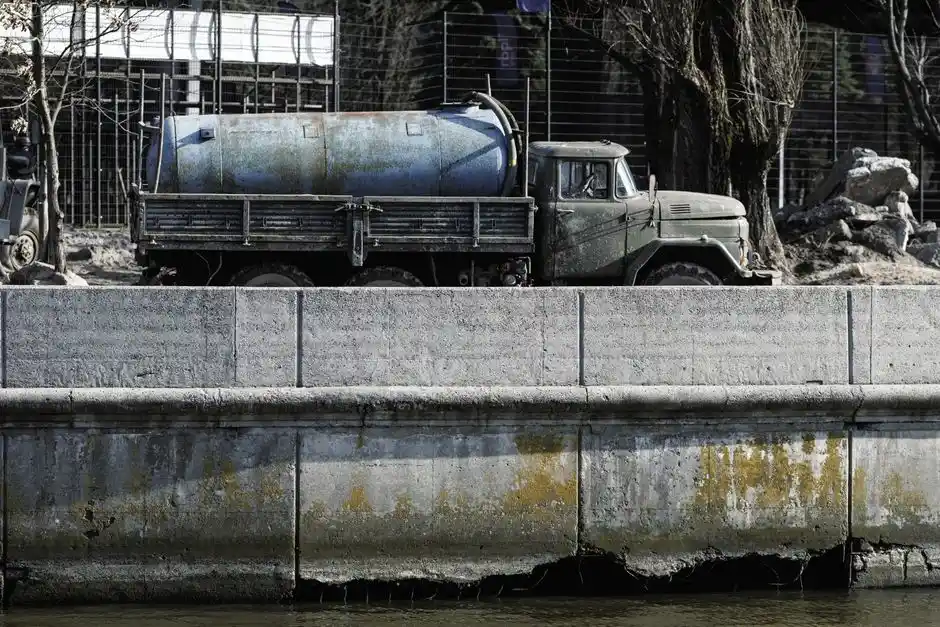 A vintage cement mixer truck parked by a canal with visible signs of wear and weathering.